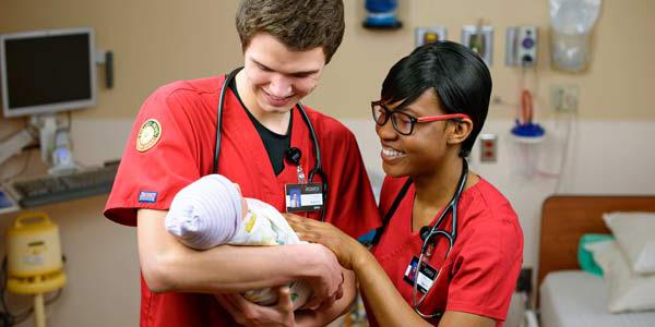 Photo of two nursing students holding a newborn.